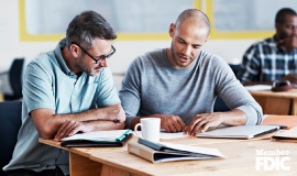 Two men are discussing and collaborating over coffee and work in a modern-looking office.