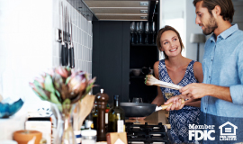 A woman stares admiringly at her husband as they cook a meal in their beautiful kitchen.