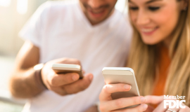 A young man and woman are showing each other their cell phone screens.