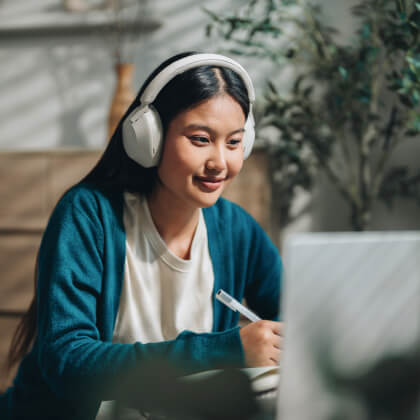 A young woman wearing headphones and looking at a laptop