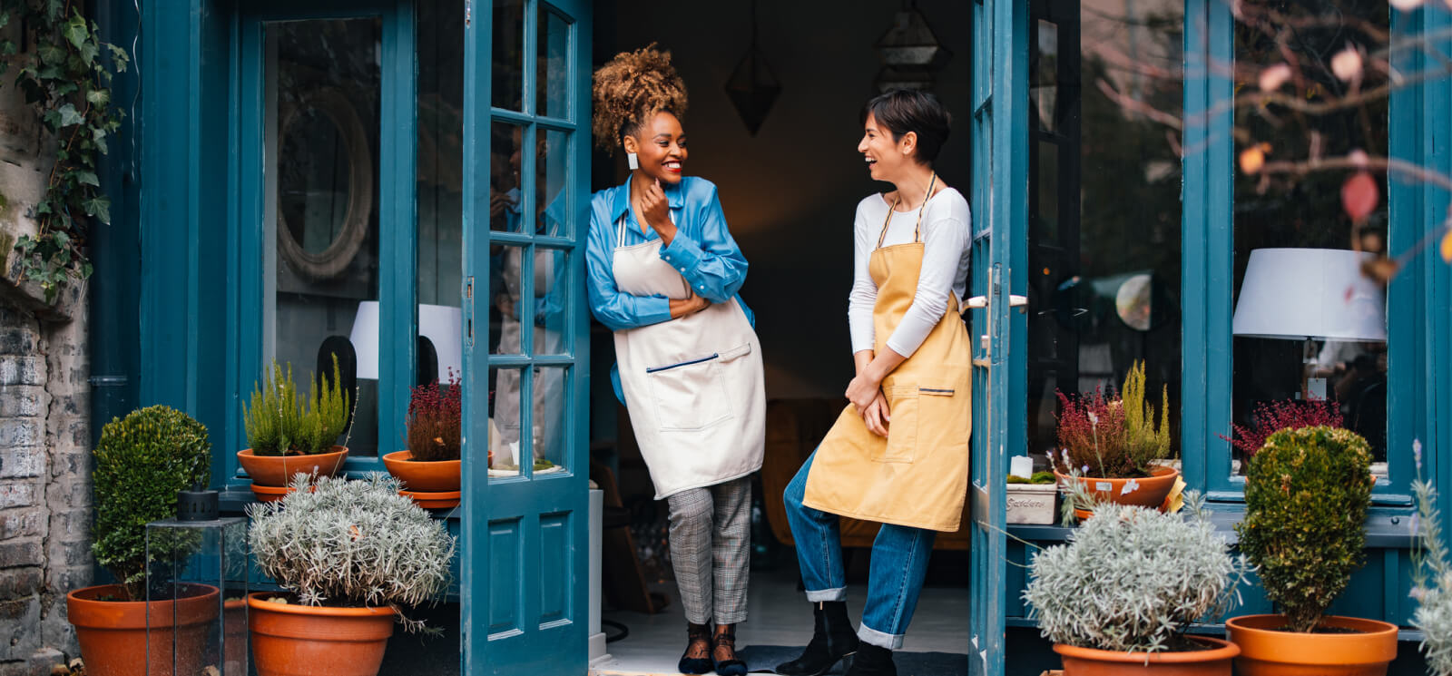Two women in aprons standing in the doorway of a small shop 