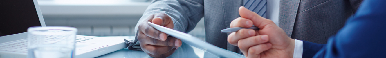 Two suited business men are reviewing information on a tablet device while at a conference table. 